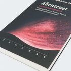 Texts: "Abenteuer", "Vob der Unverfügbarkeit", "herausgegeben von Barbara Bleisch und Konrad Paul Liessmann", "ZSOLNAY". Cover zeigt abstrakte Kunst mit rosa und schwarzen Wellen.
