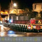 Ein Kalender mit gelbem und grauem Text. Ein nächtliches Transportszenario mit einem großen Schwerlast-Lkw auf der Straße.