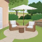 Zwei Sessel und ein Tisch unter einem weißen Sonnenschirm im Garten vor einem Haus, umgeben von Bäumen und Sträuchern.