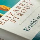 ELIZABETH STROUT, Erzähl mir alles. Illustration einer stehenden Figur mit Hut in Gelb und Blau.