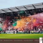 03 2027 März. Zuschauertribüne mit buntem Rauch und Fahnen, Fußballspieler auf dem Spielfeld.