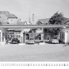 Benzol- und Graphit-Logo, drei Autos an Tankstelle, alte Gebäude im Hintergrund, Kalender unten mit dem Monat März.