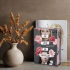 Buchcover mit "Ein Loch im Universum", Marie Döling, umgeben von rosa Blumen neben einer Vase mit trockenen Zweigen.