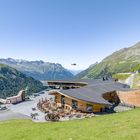 Eine moderne Holzgebirgsstation mit Terrasse, umgeben von malerischen Alpen, ein Helikopter fliegt über die Berge.