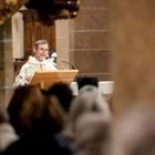 Ein Geistlicher in einer Kirche spricht zu einer Menge und steht hinter einem Lesepult.