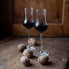 Zwei Gläser mit schwarzer Flüssigkeit stehen auf einem Holztisch, umgeben von mehreren Walnüssen.