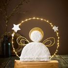 Ein Engel aus Stoff mit goldener Aura, steht auf Holz; ornamental mit Sternen und Glühlichtern verziert.