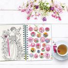 Zeichnung einer Frau mit Blumen, daneben farbige Blumenillustrationen in einem Notizbuch, Tee und rosa Blüten.