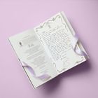 Ein aufgeschlagenes Buch mit handgeschriebenem Brief auf der rechten Seite, dekoriert mit lila Bändern.