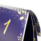 Spiralgebundener Kalender mit großer goldener Zahl 1 auf dunkelblauem Hintergrund, verziert mit goldenen Blättern und Beeren.