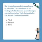 Quiztext über Bayerns Symboltier, Auswahl: a) Wolf, b) Leopard, c) Löwe. Rechts ein Dirndl, oben links Wimpel.