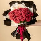 Ein großer Strauß mit gehäkelten roten Rosen, eingewickelt in schwarzen Folie und hellem Papier, mit roter Schleife.