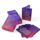 "Das Orakel der Wünsche" steht auf einer Schachtel und einem Booklet, umgeben von Karten in Lila mit goldenen Mustern.