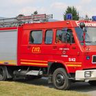 "Feuerwehr", "112", "Stadt Baunatal", "Feuerwehr", "5/42". Rotes Feuerwehrfahrzeug, seitlich gezeigt, auf einer Wiese.