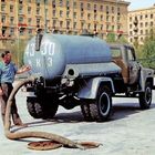 Auf einem Platz steht ein Lastwagen mit einem großen Tank. Ein Mann hält einen Schlauch, der in einen Gully führt.