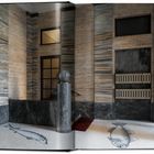 Wände aus Marmor mit grau-blauen Streifen, zwei gemalte Fische auf dem hellen Boden, rötlicher Teppich, moderne Architektur.