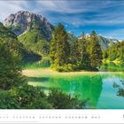 MÄRZ. Eine idyllische Landschaft mit smaragdgrünem See, umgeben von Bergen und Tannen, unter blauem Himmel.