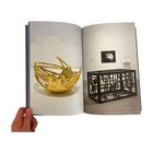 Eine goldene, filigrane Skulptur und ein schwarzes Gitterwerk im Ausstellungsraum. Links ein Buch, gehalten von einer Hand.