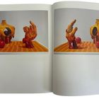 Das Bild zeigt zwei keramische Skulpturen: eine torsoähnliche Form und eine Hand, auf einem orange gepunkteten Tisch.