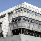 Ein modernes Gebäude mit geschwungenen, metallischen Strukturen, umgeben von einer urbanen Landschaft.