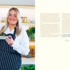 Ida Marie in gestreifter Schürze hält eine Schüssel. Sie lächelt in einer modernen Küche. Text beschreibt ihr drittes Kochbuch.