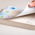 Text: "Glückskalender". Ein Kalender mit einer Hand, die eine Seite umblättert. Bunte Illustrationen auf dem Deckblatt.