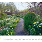 Kalenderseite: Oben ein Weg durch einen blühenden Frühlingsgarten, gesäumt von bunten Blumen und Bäumen.