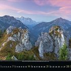 März 2024, Kalender mit Berglandschaft: Felsige Gipfel, bewaldete Hänge, rosafarbener Himmel in der Dämmerung.