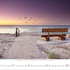 März 2022. Kalenderblatt mit Sandweg, Bank und Meer im Sonnenuntergang. Vögel fliegen am Himmel.