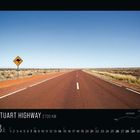 STUART HIGHWAY 2720 KM. Straße durch trockene Landschaft unter blauem Himmel, Känguru-Warnschild am Straßenrand.