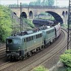 Zwei grüne Lokomotiven 140 798-0 auf Gleisen, ziehen Güterwaggons unter einer alten Steinbrücke hindurch.