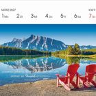 Kalender: März 2027, KW 9. Zitat: „Wenn wir an die schönsten Tage unseres Lebens denken, werden wir uns immer an Freunde erinnern.“ - Thomas Wolfe. Zwei rote Stühle am See vor Bergen.