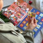 Text: "Dann ist jede Überraschung perfekt!". Eine Person hält ein buntes Bild vor einem Adventskalender.