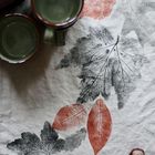 Keramikgeschirr auf einem bedruckten Stofftuch mit herbstlichen Blattmotiven in Rot und Schwarz, zwei Kastanien.