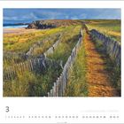 La Côte Sauvage, Halbinsel Quiberon. Ein sandiger Pfad führt durch eine grüne Landschaft mit Holzzäunen, Meer im Hintergrund.