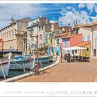 Monat 3; Morgens, Bouches-du-Rhône; Fabrigne am Kanal mit bunten Gebäuden, Booten und Café mit Sonnenschirm.