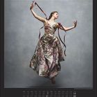 Kalender für März mit Daten, Tänzerin in floralem Kleid, schwebend vor grauem Hintergrund, elegante Pose.