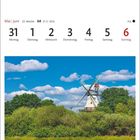 22. Woche, 21.5.–20.6., Montag 31 bis Sonntag 6. Ebkensche Mühle in Barßel im Oldenburger Münsterland. Eine Windmühle steht vor einem blauen Himmel mit weißen Wolken, umgeben von grünen Bäumen und Büschen.