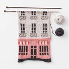 Eine Strickarbeit zeigt ein Motiv eines Hauses, mit rosa Erdgeschoss und grauem Obergeschoss.