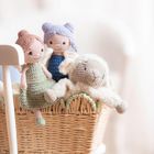 Drei gehäkelte Figuren: zwei Puppen und ein Schaf, sitzen in einem geflochtenen Korb auf einem weißen Stuhl.