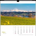Kalenderseite: März. Gelbes Feld, See, grüne Hügel und schneebedeckte Berge im Hintergrund.
