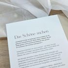 "Das Schöne suchen": Buchtext über Schönheit und Trost mit Zitaten und Gedanken. Hintergrunddetails: heller Stoff auf Holz.