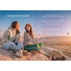 "Ein Geschenk von Gott" Text neben einem lächelnden Paar auf einem Felsen, dahinter zahlreiche Heißluftballons im Himmel.