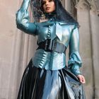 Keine Texte. Eine Person in glänzendem blauen Outfit, mit schwarzem Spitzenschleier, steht vor einer gotischen Architektur.