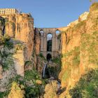 Ein großer Steinbogen überspannt eine tiefe Schlucht. Unten fließt ein Wasserfall, umgeben von Felsen und grüner Vegetation.
