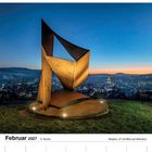 Februar 2027, 6. Woche; Rosenmontag 8, Fastnacht 9, Aschermittwoch 10. Skulptur „A“ mit Blick auf eine Stadt bei Sonnenuntergang.