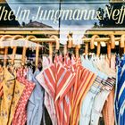 "Wilhelm Jungmann & Neffe" auf einem Schild, darunter bunte Hemden in einem Schaufenster mit braunen Holzbügeln.