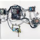 Eine Wandinstallation: Verschiedene Computerplatinen sind durch Kabel verbunden. Ein Bildschirm zeigt ein digitales Kunstwerk.