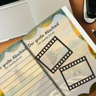 Text: "Der große Abschied – Das wünsche ich mir." Ein geöffnetes Notizbuch mit Filmstreifen-Illustrationen, daneben ein Laptop.