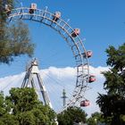 Ein großes Riesenrad mit roten Gondeln vor einem klaren blauen Himmel, umgeben von grünen Bäumen.